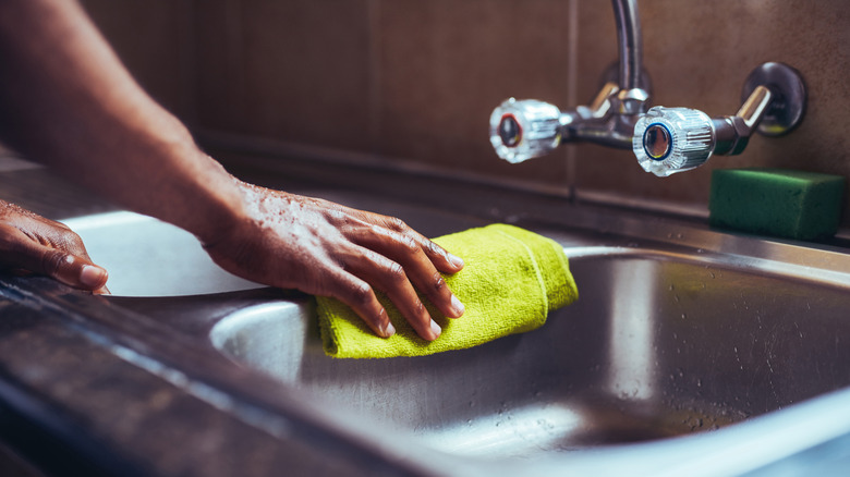 A person's hand cleaning a sink with a rag