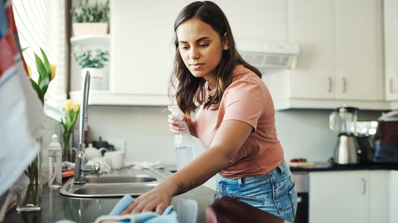 Woman cleans kitchen counter with clear spray bottle
