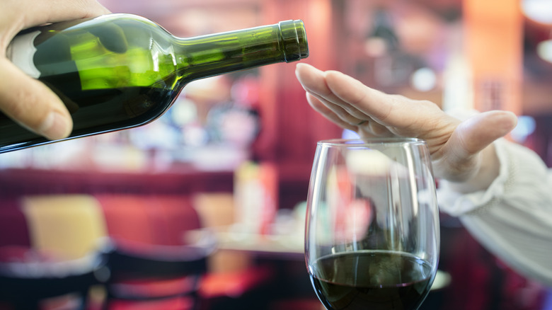 person holding a hand over a wine glass to prevent someone else from pouting them more from a bottle