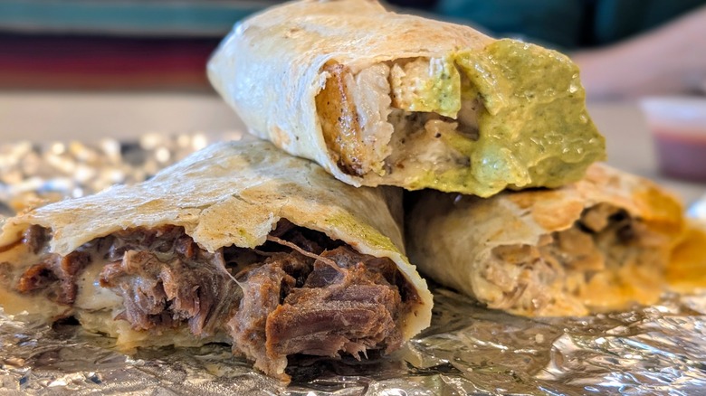 A close-up of three half-eaten burritos stacked on top of each other on a piece of tin foil
