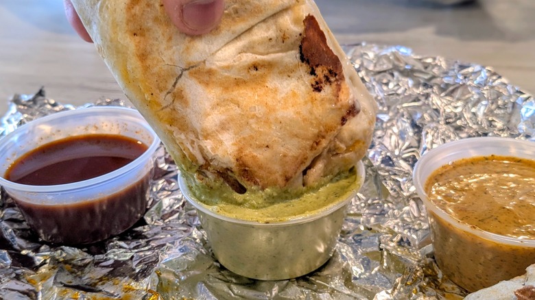 A close-up of a hand dunking a mini burrito into a cup of green sauce