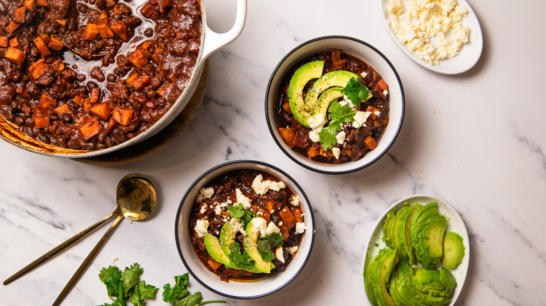 Pot of chili alongside two dressed bowls