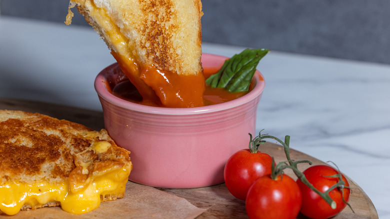 A grilled cheese sandwich being dipped into a bowl of tomato soup