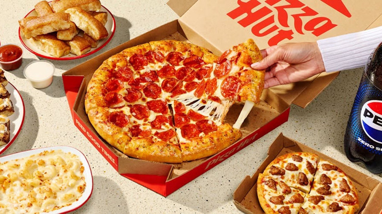 A Pizza Hut pizza in box with personal size and breadsticks and pasta with soda bottle