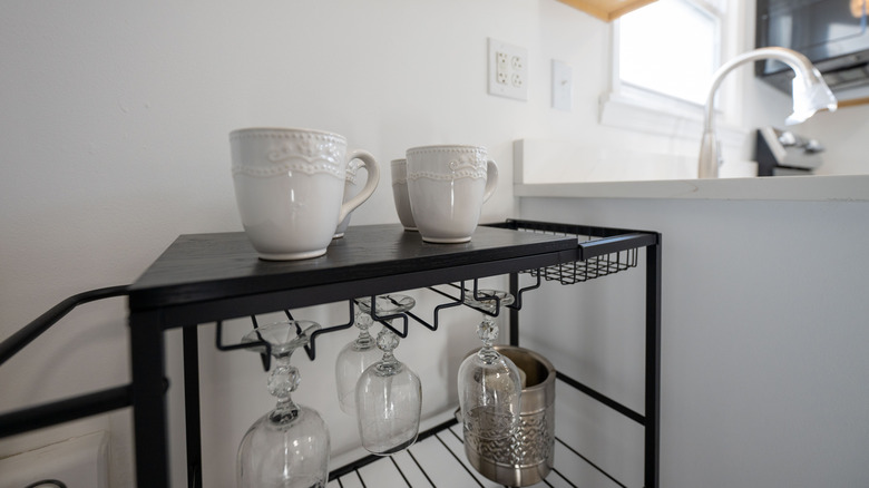 White mugs on a black metal bar cart next to kitchen counter