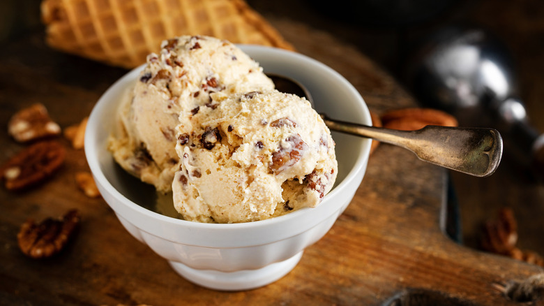 Scoops of butter pecan ice cream in a white bowl with a metal spoon