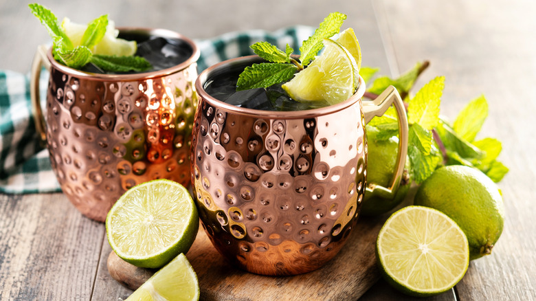 Two copper mugs full of a mixed drink with lime and mint garnish and limes and mint on the table