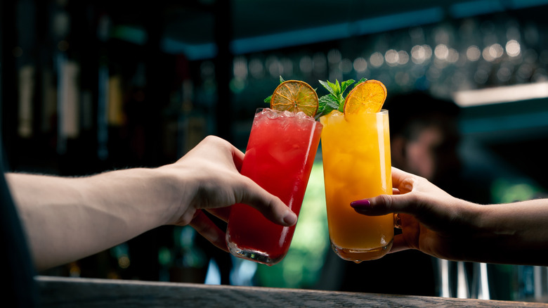Two people's hands clinking cocktail glasses