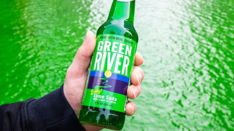 Hand holding a bottle of Green River soda in front of a green river