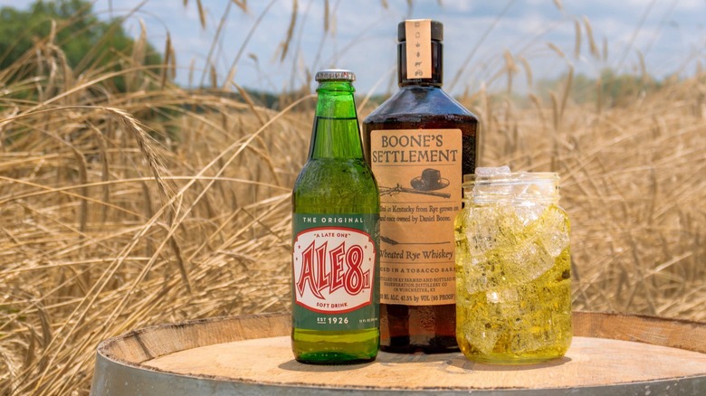 Bottle of Ale-8-One with a glass and bottle of whiskey on a barrel in a wheat field