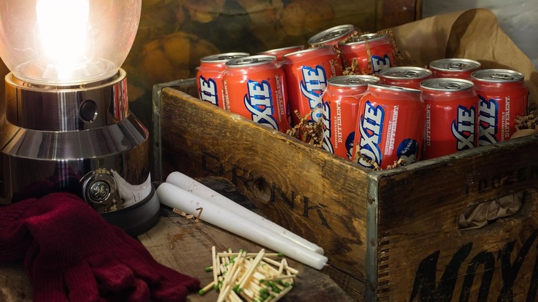 Wooden crate filled with Moxie cans next to candles, an oil lantern, and matches