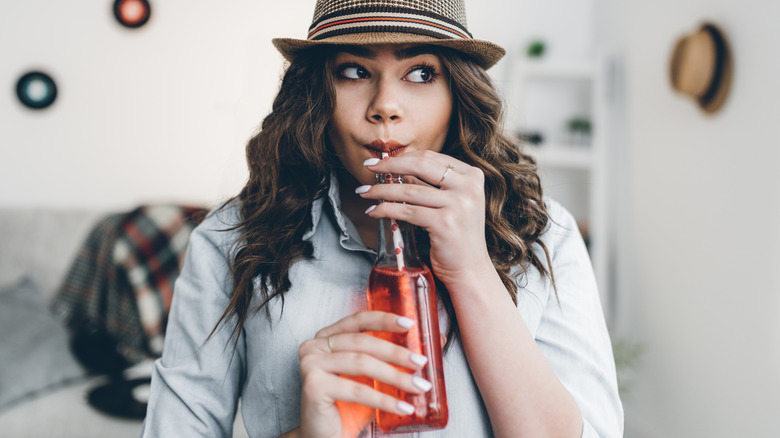 Woman in a hat drinking from a bottle of red soda