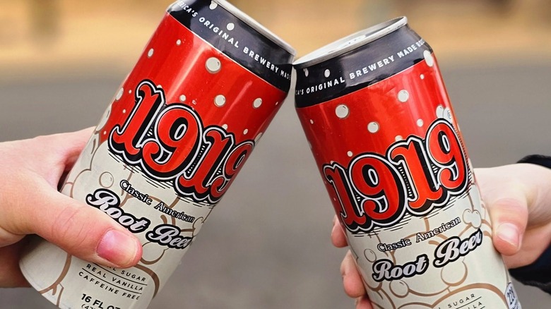 Two hands holding cans of 1919 Root Beer and toasting