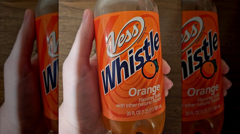 Hand holding a bottle of Vess Whistle orange