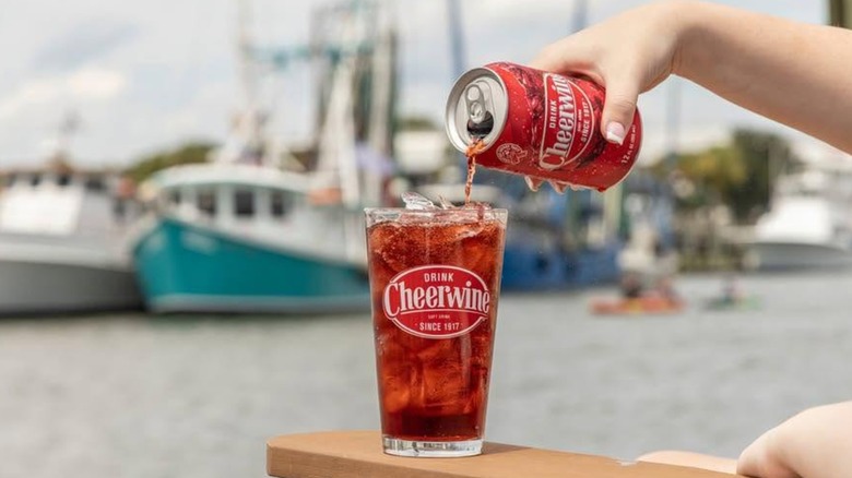 Person pouring a can of Cheerwine into a glass with a blurred marina background