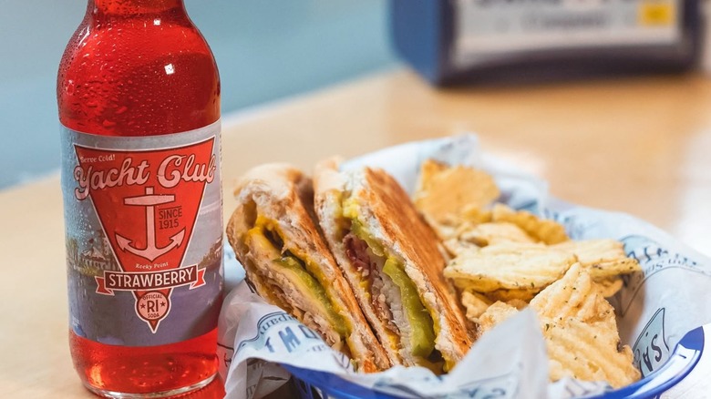 Bottle of Yacht Club strawberry soda with a sandwich and potato chips