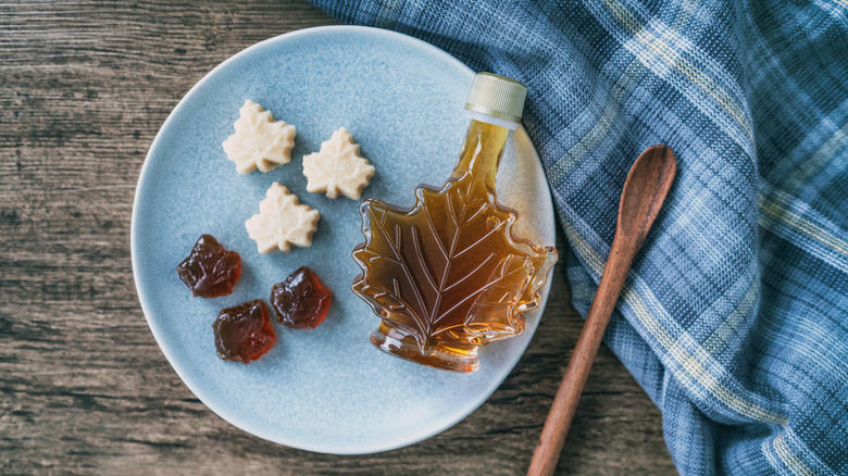 Bottle of maple syrup next to maple candies on blue plate