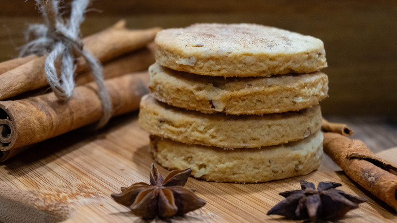 Four biscochitos stacked next to anise and cinnamon sticks on cutting board