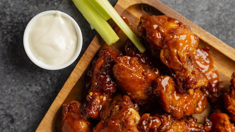 Buffalo wings on wooden plate next to celery and dipping sauce
