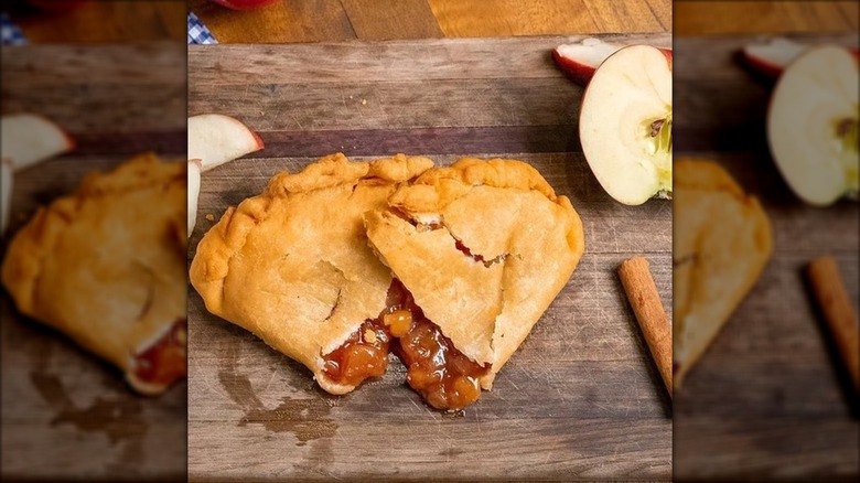 Fried apple pie cut in half next to apples on wooden cutting board