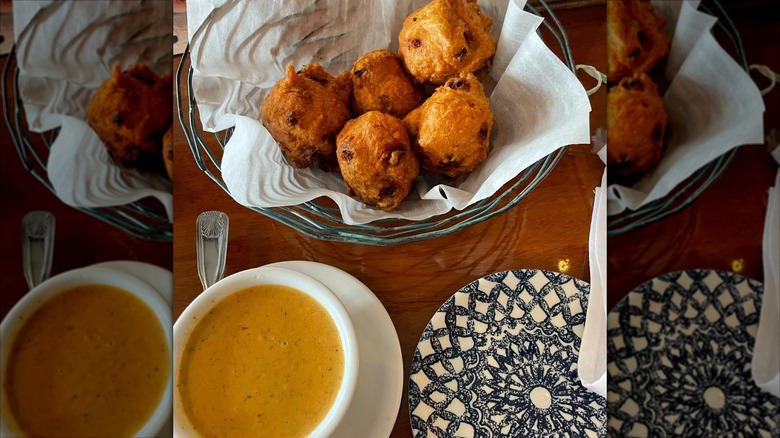 Basket of clam cakes next to lobster bisque on wooden table