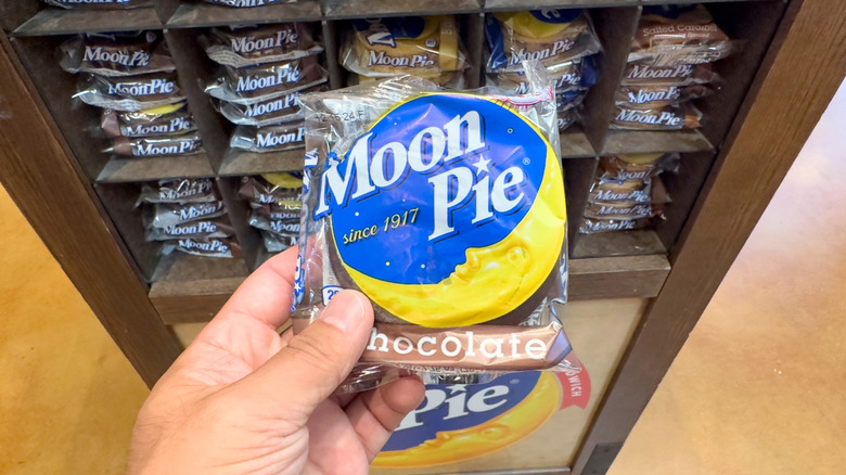 Hand holding packaged moon pie in front of shelves of moon pies