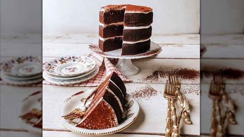 Sweet Laurel Bakery vegan keto chocolate cake on a cake stand with one slice on a plate