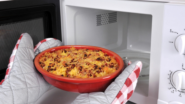 Person with oven mitts removing hot plate of food from microwave