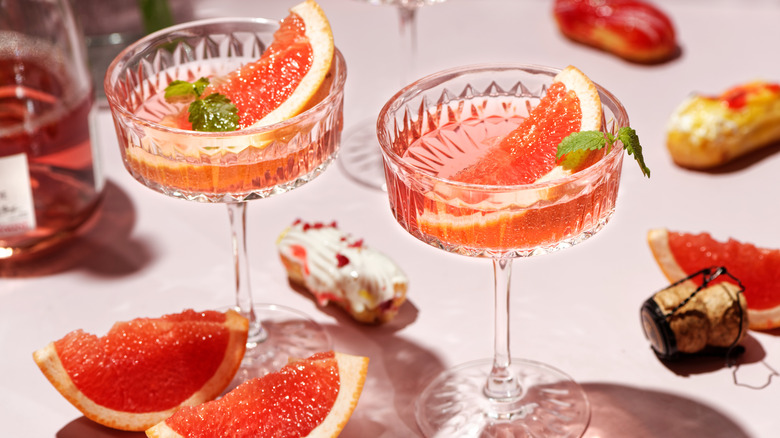 two coupe glasses filled with sparkling pink wine, grapefruit slices, and sprigs of mint