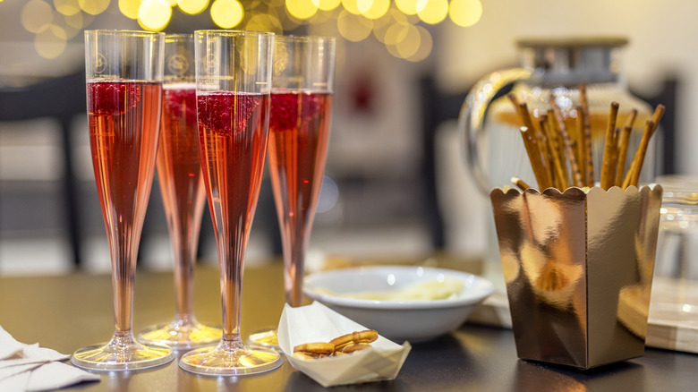 Four flutes of pink-tinged champagne with strawberries floating in them on a celebratory table