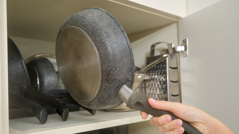 Person placing pan in a horizontal pan storage rack in a kitchen cabinet.