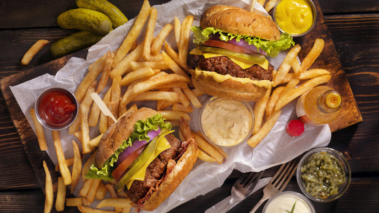 two burgers surrounded by fries and sauces