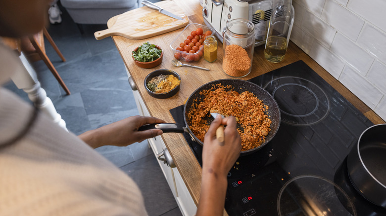 A person dry-sautees red lentils in a frying pan, with spices next to the stove