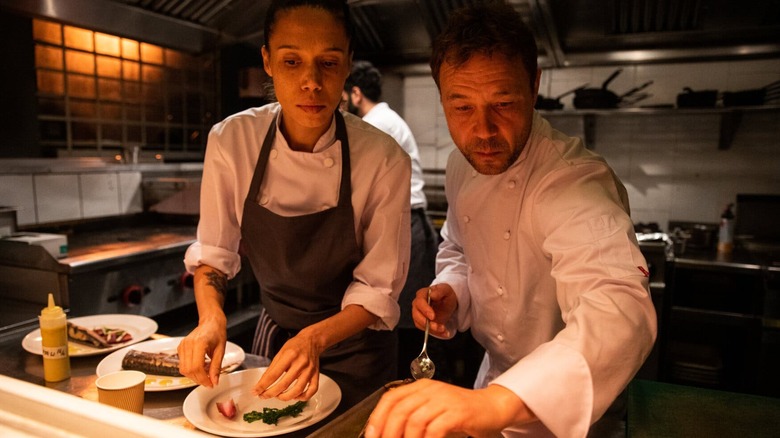 A still from "Boiling Point" depicting Andy and Carly in chef's whites preparing a dish