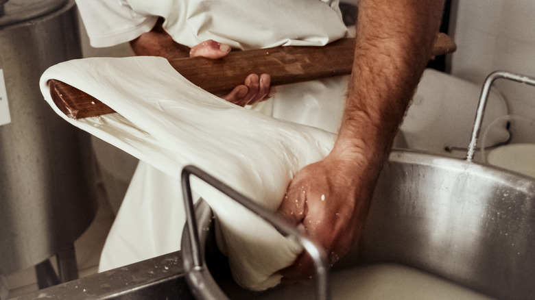 Hands stretching sheet of mozzarella with wooden paddle
