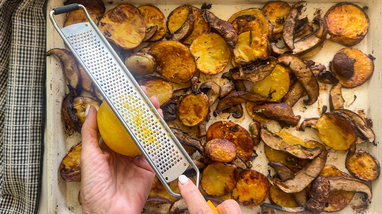hand zesting lemon over mushroom potato bake in pan