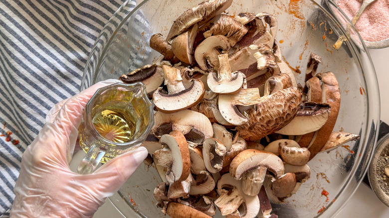 hand adding oil to bowl with sliced mushrooms