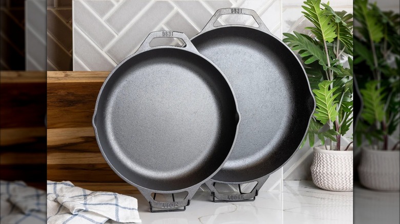 Two Lodge brand cast iron pans balanced upright on marble surface