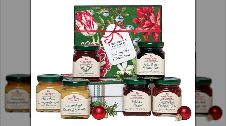 Six jars of preserves and condiments from Stonewall Kitchen brand arranged around floral print green box
