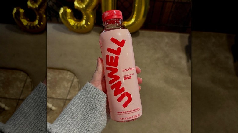 hand holding a bottle of Unwell Hydration strawberry flavor