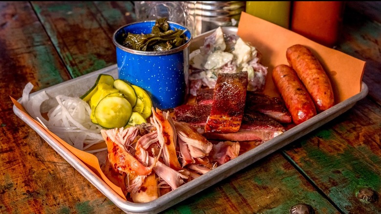 Tray of BBQ with collard greens, pickles, potato salad, and onions
