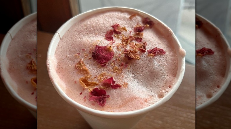 Foamy pink drink in a white cup with dried edible dark pink and orange flower petals sprinkled on top