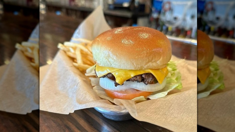 Burger with melty American cheese, onion, lettuce, and tomato sitting on a tray with fries hiding behind it