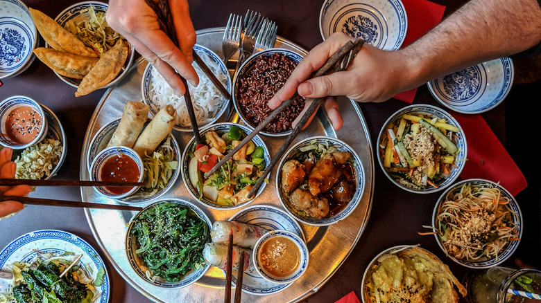 table filled with Chinese cuisine and hands reaching in with chopsticks