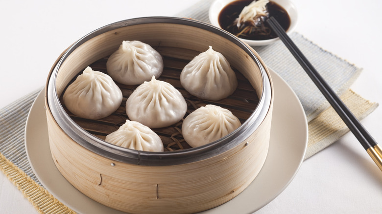 steamed dumplings in a bamboo steamer with soy sauce and chopsticks