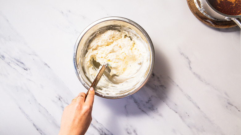 Hand stirring spatula inside bowl of Nashville hot chicken dip
