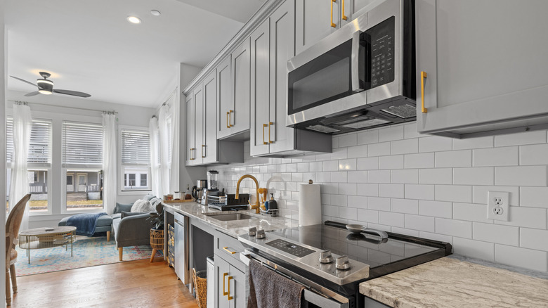 Modern kitchen with gray cabinets, brass pulls, white subway tile backsplash, and a built-in microwave over an induction range