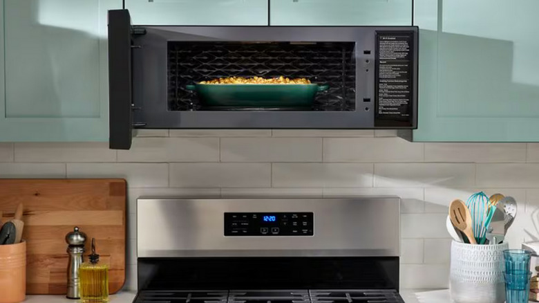Over-stove microwave in a modern kitchen with pale green cabinets and subway tile backsplash