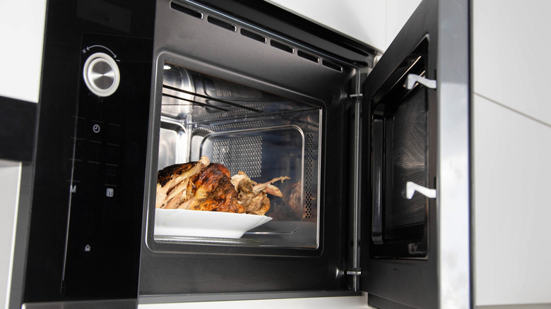 A plate of roasted chicken shown inside a combination microwave/broiler oven that's wall-mounted