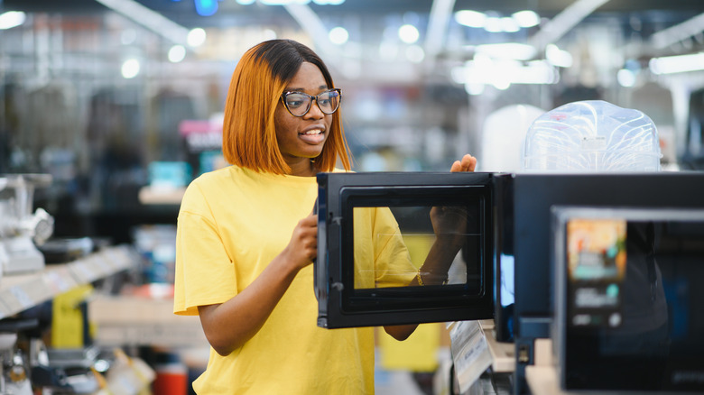African-American woman with glasses looking at microwaves in a large retail store